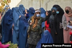 FILE - A Taliban fighter (C) stands guard as women wait in a line during a World Food Program cash distribution in Kabul, Nov. 29, 2021. (Photo by Hector RETAMAL / AFP)