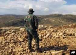 FILE - A Hezbollah fighter looks toward Syria while standing in the fields of the Lebanese border village of Brital, May 9, 2015.