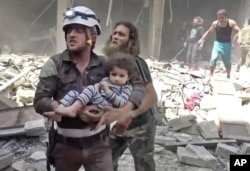 FILE - In this image made from video and posted online from Validated UGC, a Civil Defense worker carries a child after airstrikes hit Aleppo, Syria, April 28, 2016.