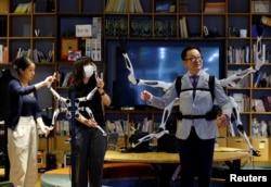 Staff members control the robot arm control unit which is synced with wearable robot arms "Jizai Arms" which Masahiko Inami of the University of Tokyo wears during its demonstration at the school's lab in Tokyo, Japan, June 22, 2023. (REUTERS/Kim Kyung-Hoon)