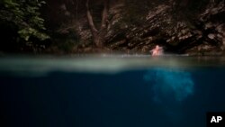 FILE - A man jumps into a spring where it meets the Vjosa River in the Kelcyre Gorge, Albania, June 24, 2019. Albania’s government has set in motion plans to dam the Vjosa and its tributaries to generate much-needed electricity.