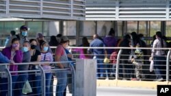 Travelers, left, waiting in line to cross a customs area into the United States at the McAllen-Hidalgo International Bridge look on as a group of migrants, right, are deported to Reynosa, Mexico, March 18, 2021, in Hidalgo, Texas. 