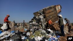 FILE - In this Aug. 27, 2014 photo, workers gather around a truck dumping trash at the Estrutual landfill in Brasilia, Brazil. The city government announced it would shut down the landfill and replace it with a new one in the district of Samambaia, located farther away from the presidential palace. (AP Photo/Eraldo Peres)