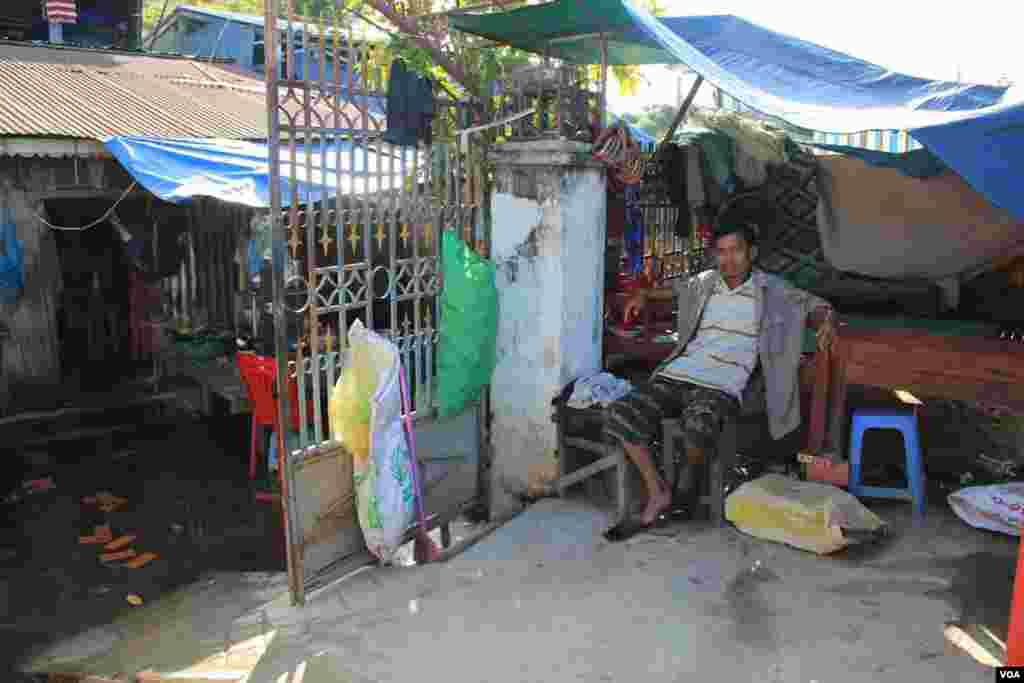 Khoeun Sovat sits on a chair in front of his house where flood waters have not receded, in Boeung Kak community in Phnom Penh, Cambodia, November 13, 2014. (Nov Povleakhena/VOA Khmer)