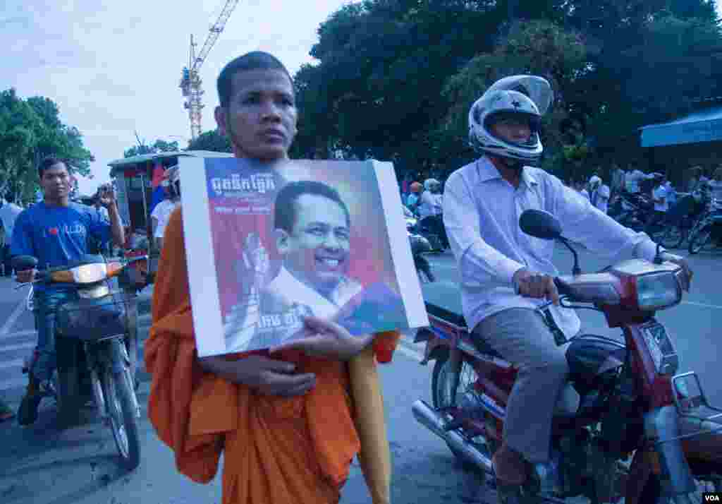 ព្រះសង្ឃព្រះពុទ្ធសាសនាមួយអង្គកាន់រូបថតលោក កែម ឡី នៅពេលចូលរួមជូនដំណើរលោក កែម ឡី នៅថ្ងៃអាទិត្យ ទី២៤ ខែកក្កដា ឆ្នាំ២០១៦នេះ។សពអ្នកវិភាគនយោបាយឯករាជ្យលោក កែម ឡី ត្រូវយកទៅបូជានៅឯស្រុកកំណើតរបស់លោកនៅស្រុកត្រាំកក់ ខេត្តតាកែវ កាលពីព្រឹកថ្ងៃអាទិត្យ។ លោកកែម ឡីត្រូវឃាតករបាញ់សម្លាប់នៅថ្ងៃទី ១០កក្ដដា កន្លងទៅនេះ។ (ឡេង ឡែន/VOA)