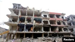 ស្រ្តី​ម្នាក់​ដើរ​កាត់​អគារ​បាក់​បែក​មួយ​ក្នុង​តំបន់​ Douma នៃ​ទីក្រុង​ Damascus ប្រទេស​ស៊ីរី កាល​ពី​ថ្ងៃ​ទី​១២ ខែ​កុម្ភៈ ឆ្នាំ​២០១៥។​