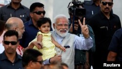 India's PM Minister Narendra Modi gestures as he holds the granddaughter of India's ruling Bharatiya Janata Party (BJP) president Amit Shah after he arrives to cast his vote at a polling station in Ahmedabad, Apr. 23, 2019. 