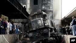 People look at a damaged train inside Ramsis train station in Cairo, Egypt, Wednesday, Feb. 27, 2019. The high-speed crash caused an explosion of the locomotive's fuel tank and triggered a huge blaze that engulfed that part of the station.