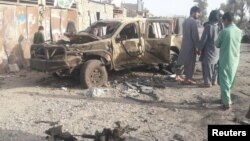 Warga berdiri di dekat kendaraan yang hancur dalam pertempuran antara pasukan Afghanistan dan militan Taliban di provinsi Farah (16/5). 