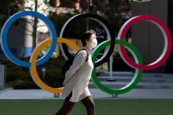 FILE - A woman wearing a protective face mask amid an outbreak of the coronavirus walks past Olympic rings displayed in front of the Japan Olympics Museum, in Tokyo, Japan, March 13, 2020.