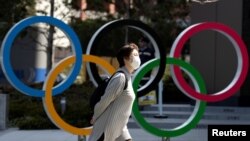 Seorang perempuan menggunakan masker pelindung berjalan melintas lambang Olimpiade, di depan Japan Olympics Museum di Tokyo, Jepang, di tengah wabah virus corona, 13 Maret 2020. (Foto: Reuters) 