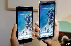 FILE - A woman holds up the Google Pixel 2 phone, left, next to the Pixel 2 XL phone at a Google event at the SFJAZZ Center in San Francisco, Oct. 4, 2017.