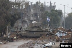 Bendera Israel berkibar di atas tank, sementara warga Palestina yang melarikan diri dari Gaza utara bergerak ke selatan selama gencatan senjata, dekat Kota Gaza 27 November 2023. (Foto: REUTERS/Ibraheem Abu Mustafa)