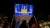 A woman sells balloons near a giant TV screen broadcasting a news of U.S. President-elect Joe Biden delivers his speech, at a shopping mall in Beijing, Nov. 8, 2020. 