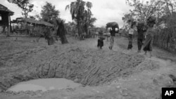 Cambodian villagers walk around bomb crater in road near embattled Takeo 42 miles southwest of Phnom Penh in Cambodia May 17, 1973.
