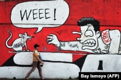 Seorang perempuan berjalan melewati tembok berhias grafiti yang menunjukkan dukungan terhadap gerakan anti orupsi di Jakarta, 20 Juli 2010. (Foto: AFP/Bay ISMOYO)