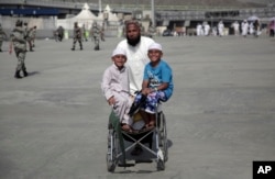 FILE - Two children pose for the camera while pushed by their father, who walks to cast stones at three huge stone pillars in the symbolic stoning of the devil, during the Hajj, outside the holy city of Mecca, Saudi Arabia, Sept. 3, 2017.