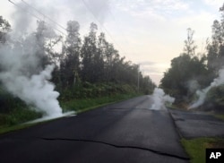 In this image released by the U.S. Geological Survey, steam rises from cracks in the road shortly before a fissure opened up on Kaupili Street in the Leilani Estates subdivision in Pahoa, Hawaii, May 4, 2018.