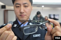 A police officer displays a pair of glasses with a hidden camera and a tiny receiver attached to a coin, which are both exam cheating equipment confiscated by the police, in Shenyang, Liaoning province in 2013. (REUTERS)