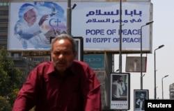 A man rides a bicycle past a billboard ahead of Pope Francis’ visit in Cairo, Egypt, April 26, 2017.