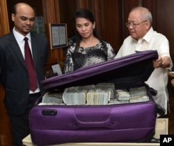 This photo provided by the Bangko Sentral ng Pilipinas, from left, Second Secretary and Head of Chancery of the Bangladesh Embassy in Manila Probash Lamarong, Anti-Money Laundering Council (AMLC) Secretariat Executive Director Julia Bacay-Abad and AMLC Member and Insurance Commissioner Emmanuel Dooc opens a bag containing US dollars that was returned by Chinese casino junket operator Kam Sin Wong to Bangladesh and Philippine AMLC officials in Manila, March 31, 2016.