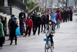 A woman wearing a face mask rides a shared bicycle past people lining up to enter a supermarket in Wuhan, Hubei province, the epicentre of China's coronavirus disease (COVID-19) outbreak, April 1, 2020.