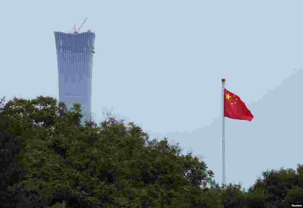 2018年6月8日，北京市中心的天安门广场飘扬着国旗。照片上的大楼是正在施工的“中国尊”，计划成为北京最高的建筑。这是中信集团总部大楼，位于北京市商务中心区。中国尊的名字来自中国古代的盛酒器皿“尊”。