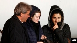 Italian aid workers, 21-year-old Greta Ramelli, center, and 20-year-old Vanessa Marzullo, right, are welcomed by Foreign Minister Paolo Gentiloni as they arrive at Ciampino's military airport, near Rome, early Friday, Jan. 16, 2015.