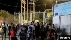 Refugees and migrants stand at the closed gate of the Moria migrant camp, after a fire at the facility, on the island of Lesbos, Greece, Sept. 19, 2016. 