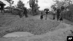 Cambodian villagers walk around bomb crater in a road near embattled Takeo 42 miles southwest of Phnom Penh in Cambodia May 17, 1973. US jets continue to support Khmer government troops against insurgent forces throughout Cambodia despite criticism and threatened congressional action to force an end to the bombing. (AP Photo/Chhor Yuthy)