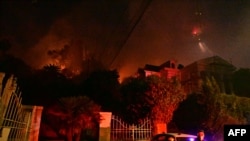 A police officer stands below burning brush at the Sunset Fire near Hollywood Blvd in the Hollywood Hills in Los Angeles, California, on January 8, 2025.