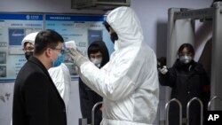 A worker wearing a hazardous materials suit takes the temperature of a passenger at the entrance to a subway station in Beijing, Jan. 26, 2020. 