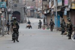 FILE - A Kashmiri municipal worker pushes a trash cart as Indian paramilitary soldiers patrol during curfew in Srinagar, India-controlled Kashmir, Aug. 6, 2019.