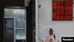 Arhiv - Žena stoji pored table na kojoj su prikazani kursevi evra i američkog dolara u odnosu na rusku rublju u Moskvi.
