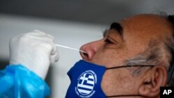 A medical staff member from the National Health Organization (EODY) conducts a rapid COVID test on a man, wearing a face mask with the Greek flag, in Athens, Nov. 5, 2020. 