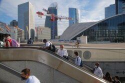 People ride an escalator as they arrive at La Defense business district while wearing a protective face masks as a precaution against the coronavirus, in Paris, Aug. 21, 2020.