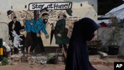 FILE - A woman wears a face mask to help curb the spread of the new coronavirus past a coronavirus awareness mural in Bekasi on the outskirts of Jakarta, Indonesia, July 29, 2020.
