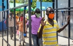 FILE - Ferry commuters walk through an automated disinfecting machine installed this week that sprays disinfectant onto all passengers boarding or disembarking ferries that cross the harbor of Mombasa, on the south coast of Kenya, April 8, 2020.
