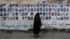 FILE - A Bahraini woman walks past images of political prisoners plastered on a wall in Sanabis, Bahrain, Oct. 22, 2015. In May 2018, the court revoked the citizenship of 115 people in a mass terrorism trial.