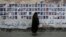 FILE - A Bahraini woman walks past images of political prisoners plastered on a wall in Sanabis, Bahrain, Oct. 22, 2015. In May 2018, the court revoked the citizenship of 115 people in a mass terrorism trial.