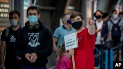 A staff member carries a sign looking for passenger from high-risk-countries at a Corona test center at the airport in Frankfurt, Germany, Friday, Aug. 7, 2020. Sign reads "home comers from high-risk-countries" .(AP Photo/Michael Probst)