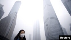 A woman wearing a mask walks past below skyscrapers amid heavy smog at the financial district of Pudong, in Shanghai, China, Dec. 11, 2015. 