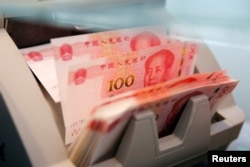 FILE - Chinese 100 yuan banknotes are seen in a counting machine while a clerk counts them at a branch of a commercial bank in Beijing, China, March 30, 2016.