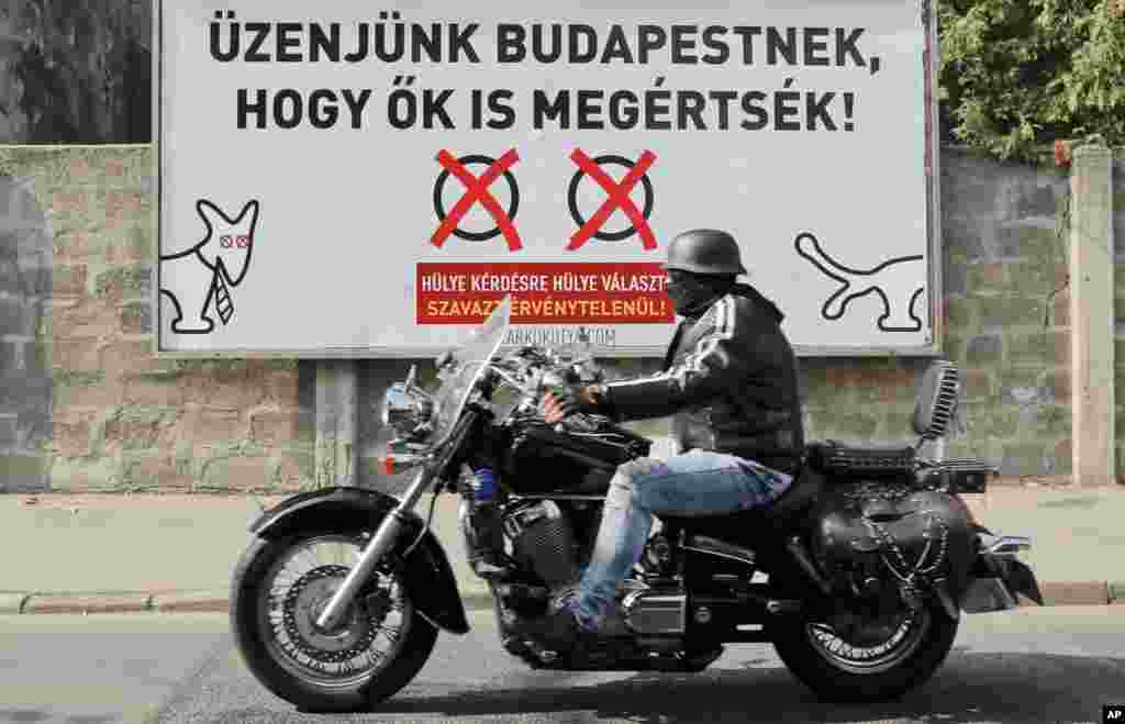 A man rides a motorcycle by a poster in opposition to Hungarian Premier Minister&#39;s Viktor Orban policies on migrants in Budapest, Oct. 1, 2016.