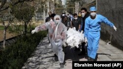 In this March 30, 2020 file photo, people wearing protective clothing carry the body of a victim who died after being infected with the new coronavirus at a cemetery just outside Tehran, Iran. (AP Photo/Ebrahim Noroozi, File)