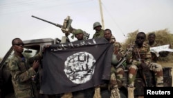 FILE- Nigerian soldiers hold up a Boko Haram flag that they had seized in the recently retaken town of Damasak, Nigeria.