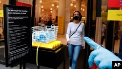 Face masks in a basket at a shop entrance as a woman wearing a face mask to protect herself from COVID-19 leaves in London, Friday, July 24, 2020. 