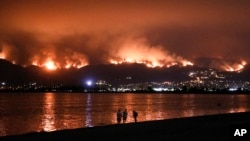 Onlookers are silhouetted against the reflection of a wildfire burning in the Cleveland National Forest in Lake Elsinore, Calif., Aug. 8, 2018. 