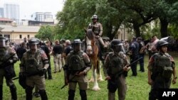 24 اپریل 2024 کو ٹیکساس کے ریاست ٹیکساس میں یونیورسٹی آف ٹیکساس کے کیمپس میں فلسطینی حامی طلباء اسرائیل-حماس جنگ کے خلاف احتجاج کرتے ہوئے ٹیکساس اسٹیٹ ٹروپرز اور قانون نافذ کرنے والے اداروں کے دیگر ارکان منظر کی نگرانی کر رہے ہیں۔