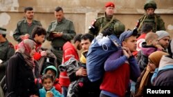 Syrian army soldiers (rear L) and Russian soldiers (rear R) look on as rebel fighters and their families evacuate the besieged Waer district in the central Syrian city of Homs, after an agreement was reached between rebels and Syria's army, March 18, 2017.